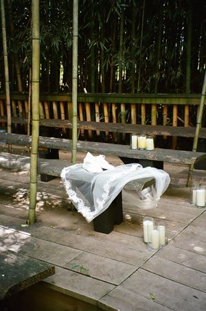 White lace fabric draped over a bench surrounded by bamboo trees and candles on a wooden deck in a serene setting.