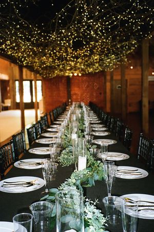 Elegant wedding reception table setting with string lights overhead and greenery centerpieces running down long dining tables.
