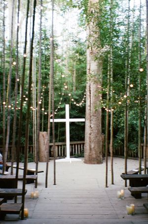An outdoor chapel in a bamboo forest with string lights and a white cross at the altar, creating a magical wedding setting.