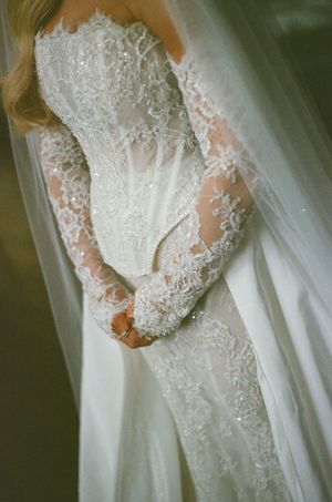 Bride in elegant long-sleeve lace wedding gown with beading and flowing veil, showcasing intricate detail.