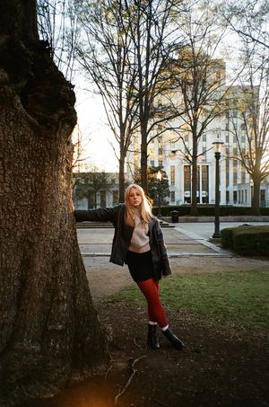 Casual portrait against a large tree trunk with building and sunlight in background.