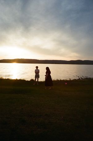 Two silhouettes stand by a lake during sunset creating a peaceful scenic moment.