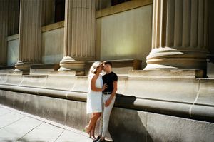 Couple sharing intimate moment against classical stone columns at night.