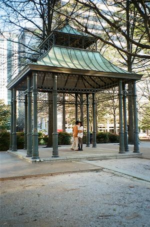 Historic metal gazebo with copper roof in urban park setting at sunset.