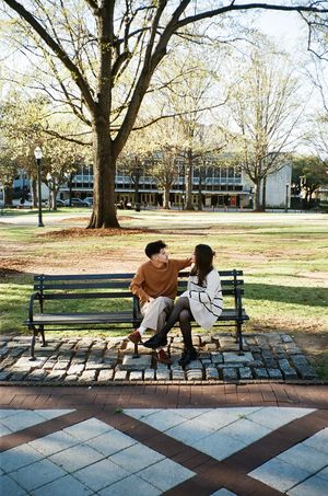 Two figures sharing a tender moment while sitting on a park bench surrounded by autumn trees.
