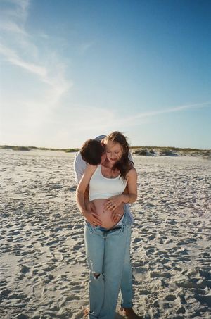 A couple embracing on a sandy beach at sunset with bright blue skies in the background.