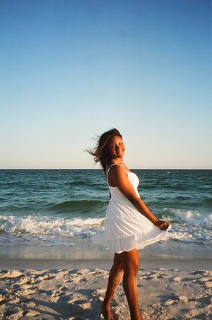 Woman in white dress twirling on beach with ocean waves in background.