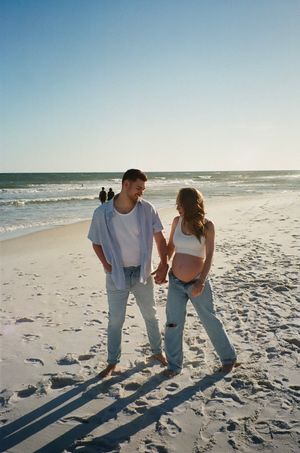 Couple walking hand in hand on a sunny beach with long shadows cast on the sand.