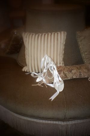 White strappy bridal shoes next to a striped throw pillow on gray furniture.