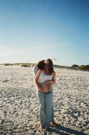 Couple shares intimate moment on sandy beach during sunset photoshoot.