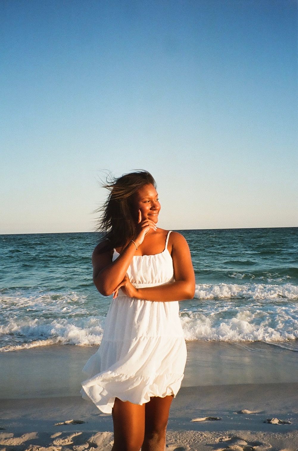 Woman in white sundress enjoying a breezy moment at the beach.