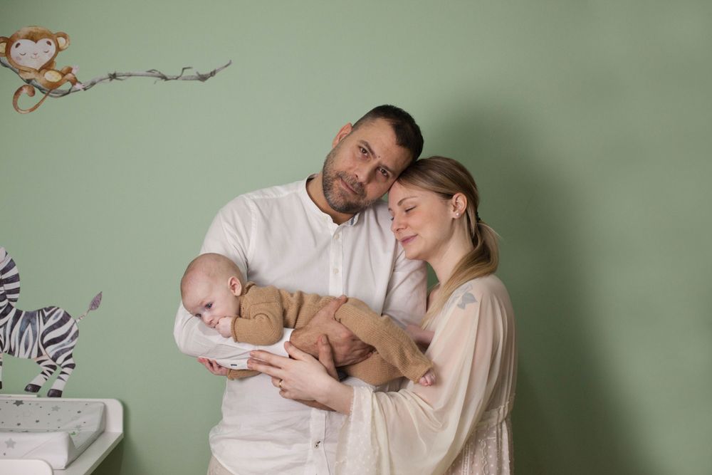 bambino in braccio a mamma e papà, genitori felici e sereni, sorrisi, sessione fotografica in casa a Peschiera Borromeo.