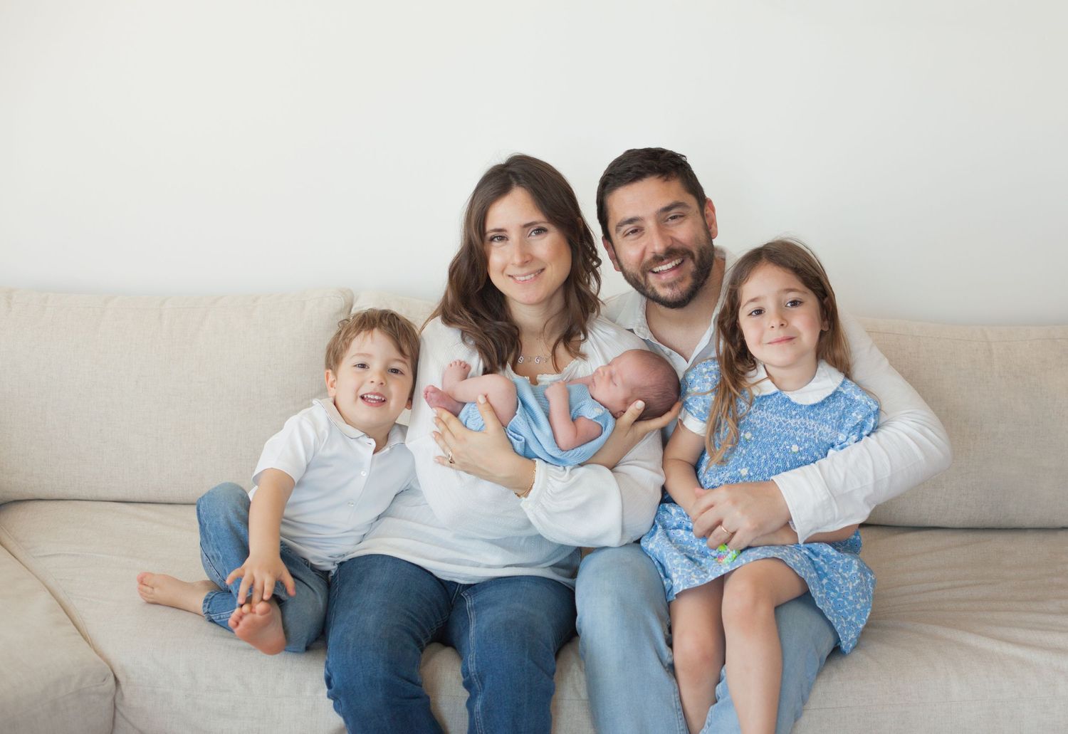 famiglia felice seduta sul divano, mamma papò neonato fratello e sorella. vestiti azzurri e blu jeans, sessione family a Milano,  Peschiera