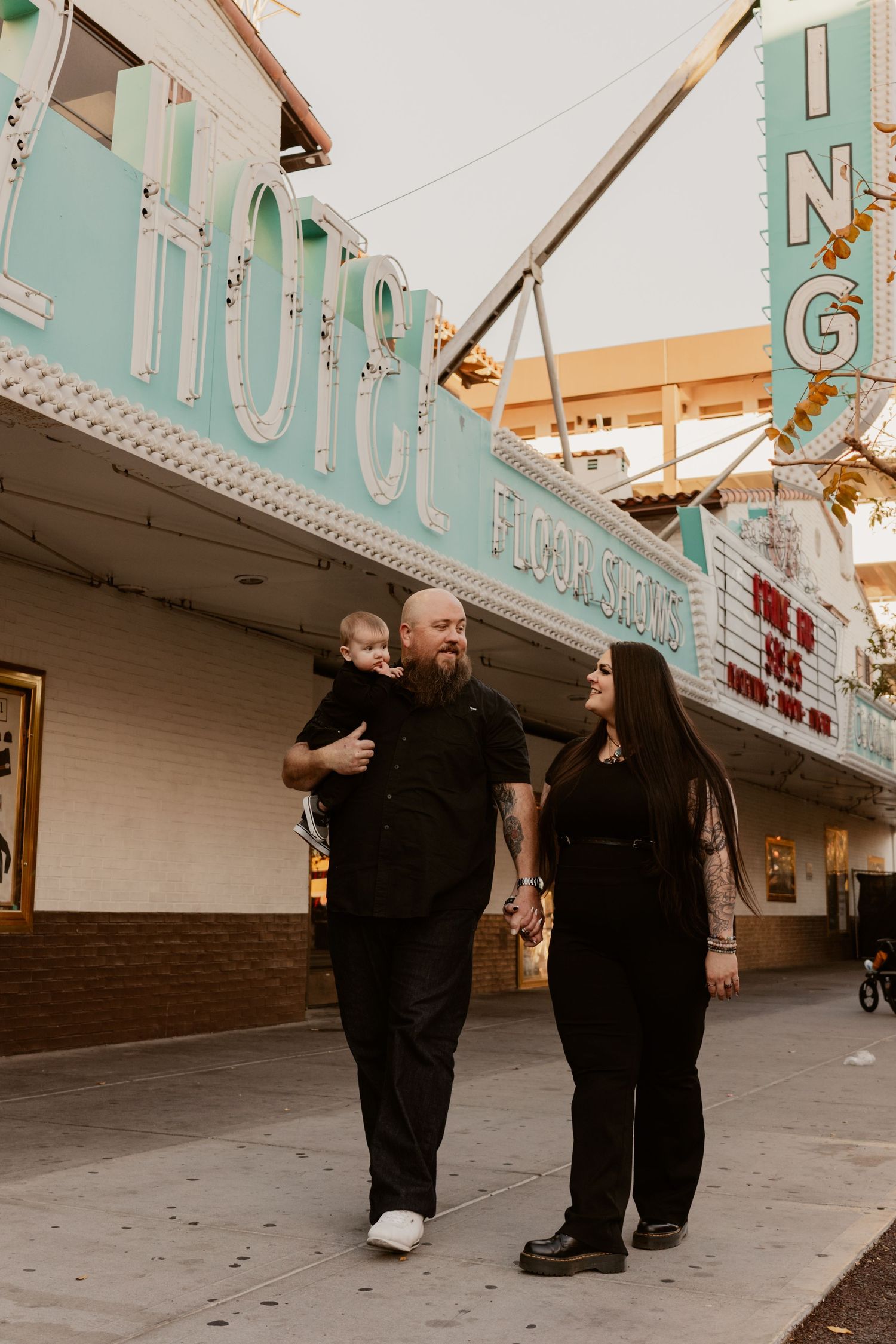 Family dressed in black walking outside vintage Hotel neon sign in Las Vegas.