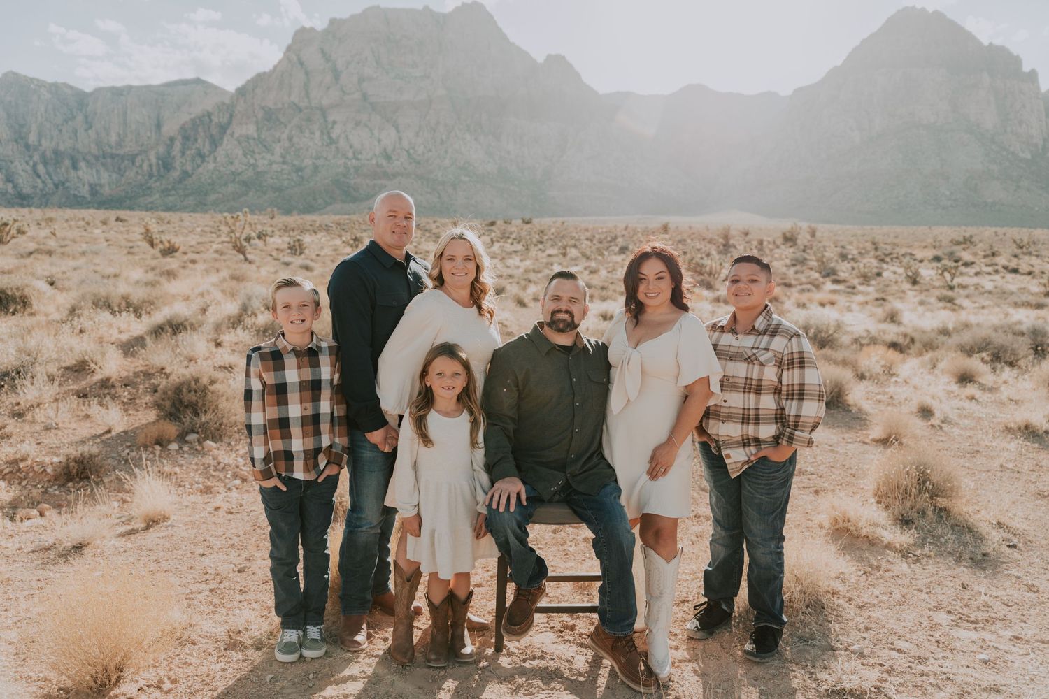 Family of seven posing together in desert landscape with mountains backdrop during golden hour.
