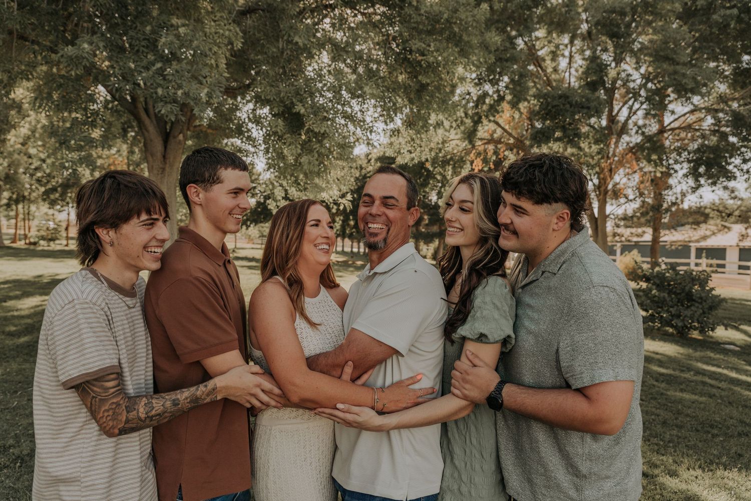 Happy family of six laughing and embracing together outdoors in a sunny park setting.