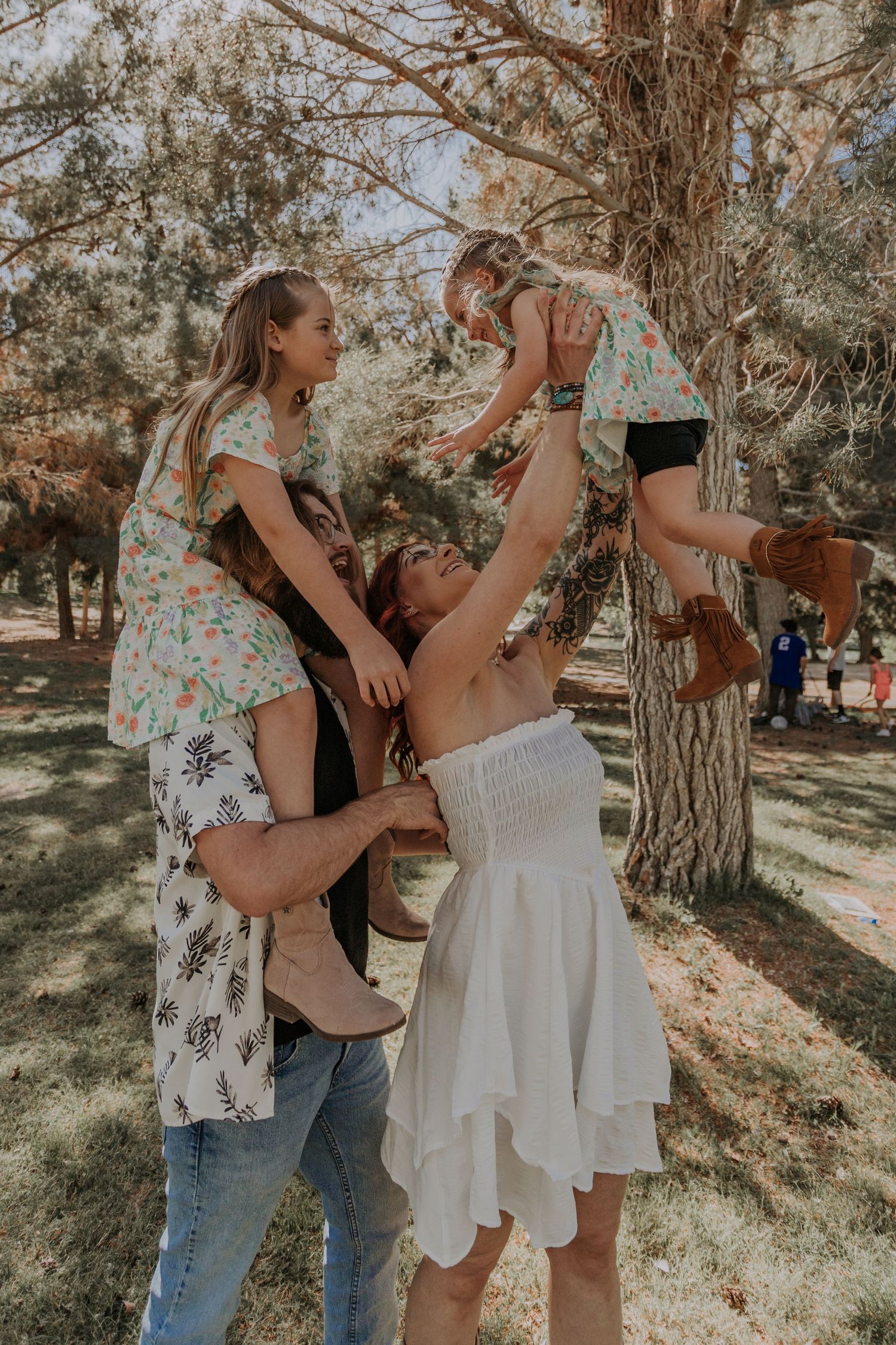 Happy family with two young daughters being lifted in the air outdoors in a park.