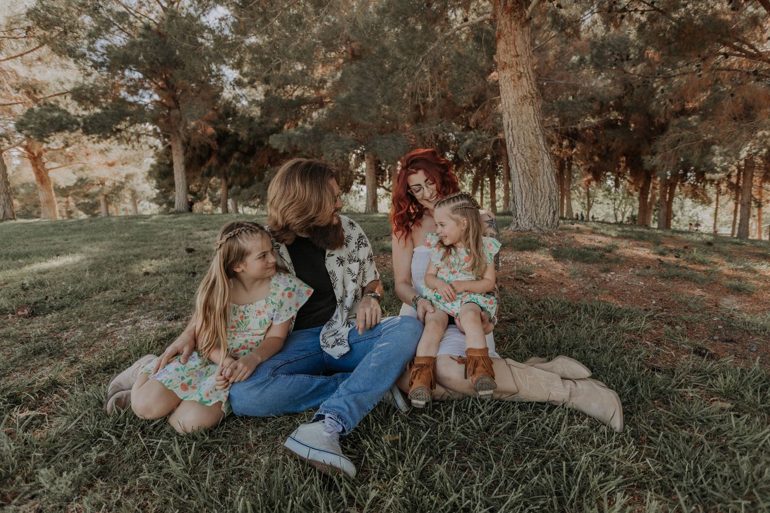 Mother and father sitting on grass with two young daughters in matching floral dresses.