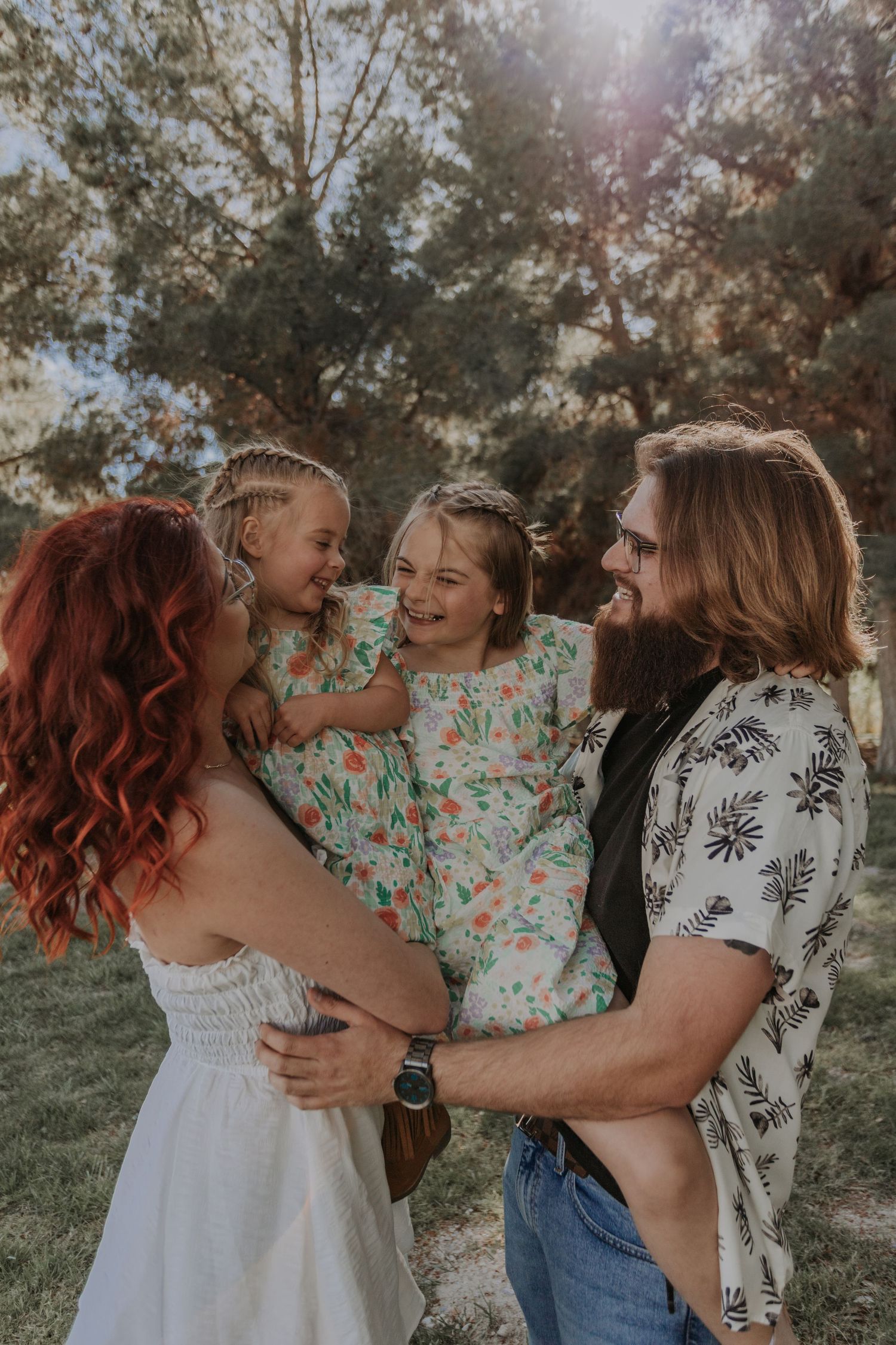 Joyful family with redhead mom, bearded dad, and two girls in matching floral dresses outdoors.