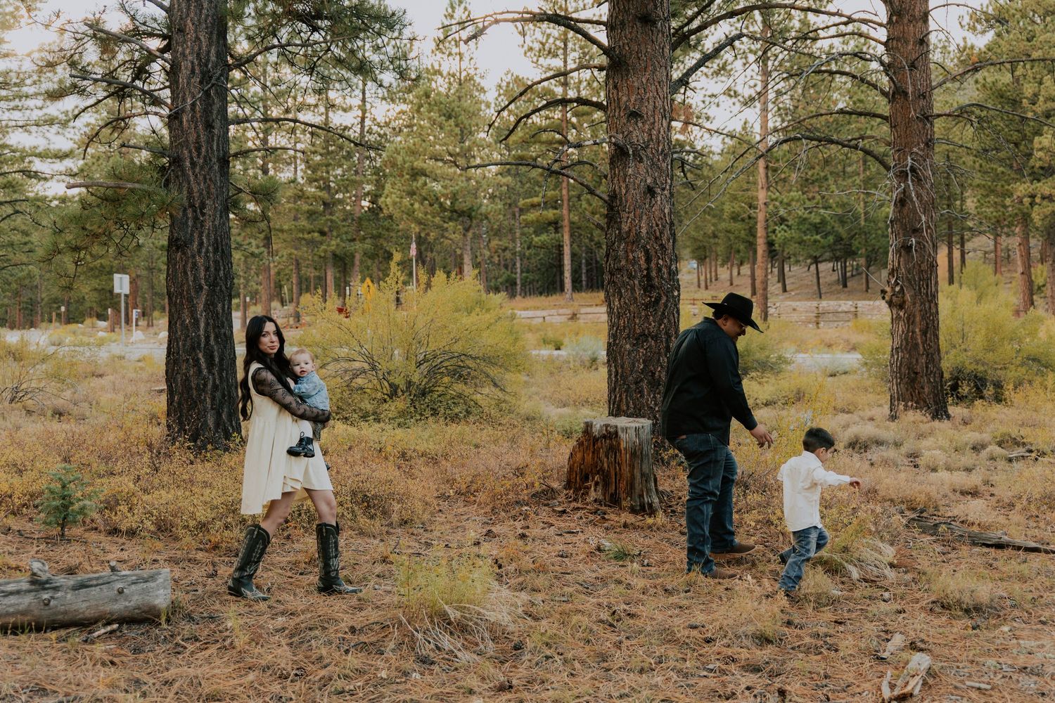 Family of four enjoying a relaxed outdoor moment among tall pine trees in an autumn forest setting.