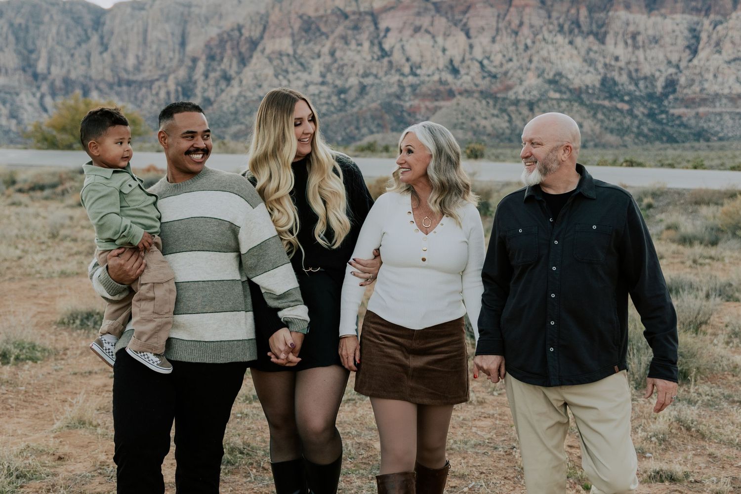 Joyful family of five posing together in a desert setting with rocky mountains in the background.