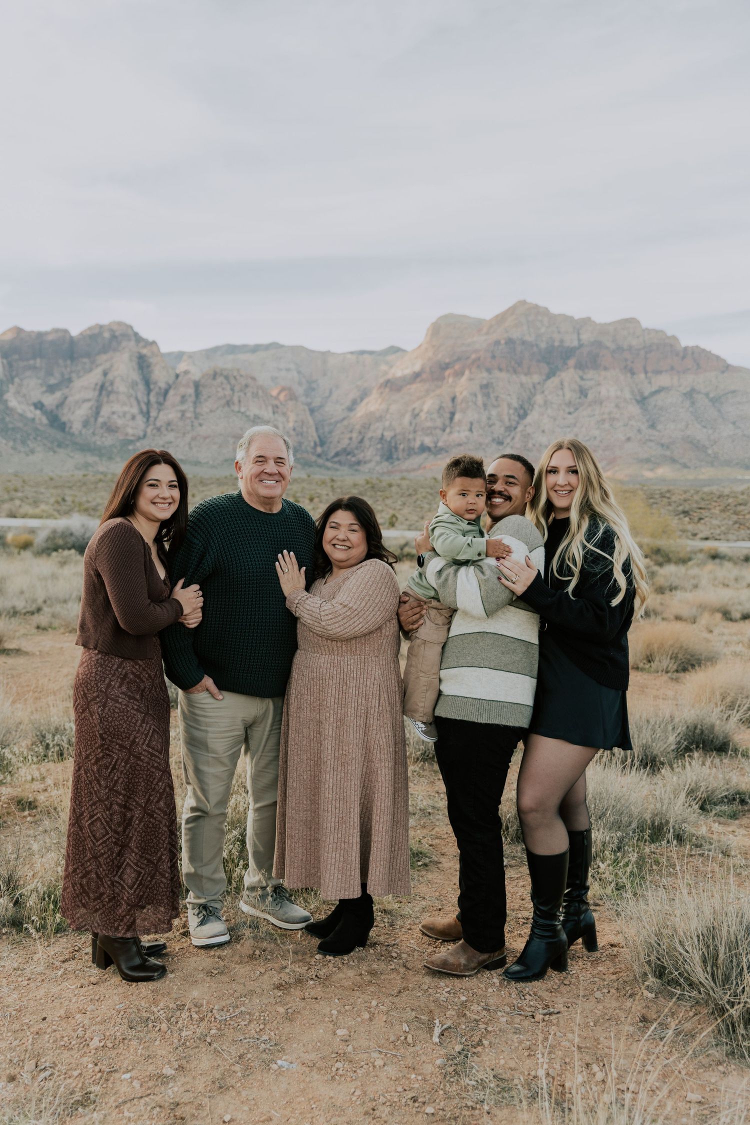 Extended multigenerational family portrait taken outdoors with stunning red rock canyon mountains behind them.