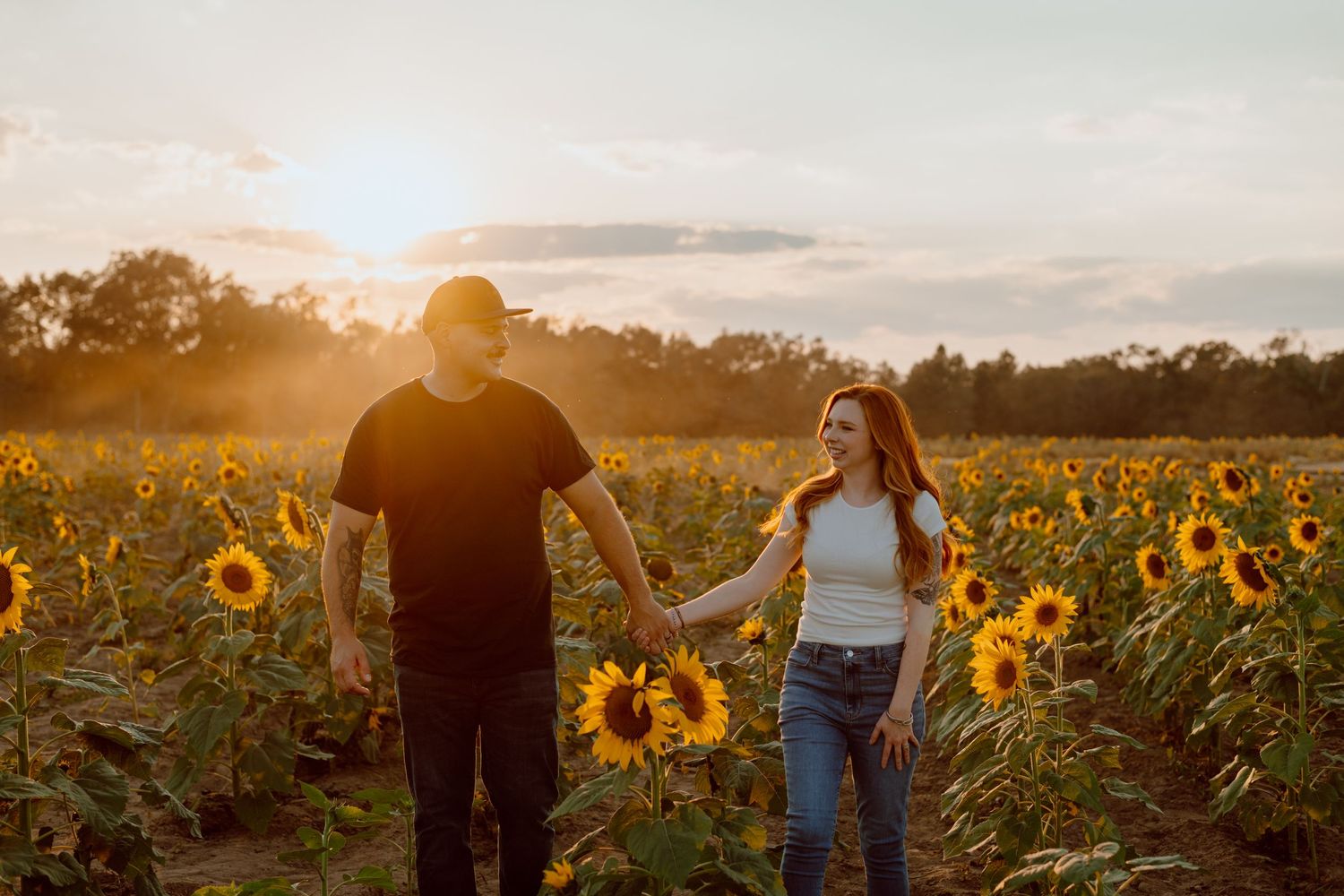 Couple walking hand in hand through vibrant sunflower field at sunset.