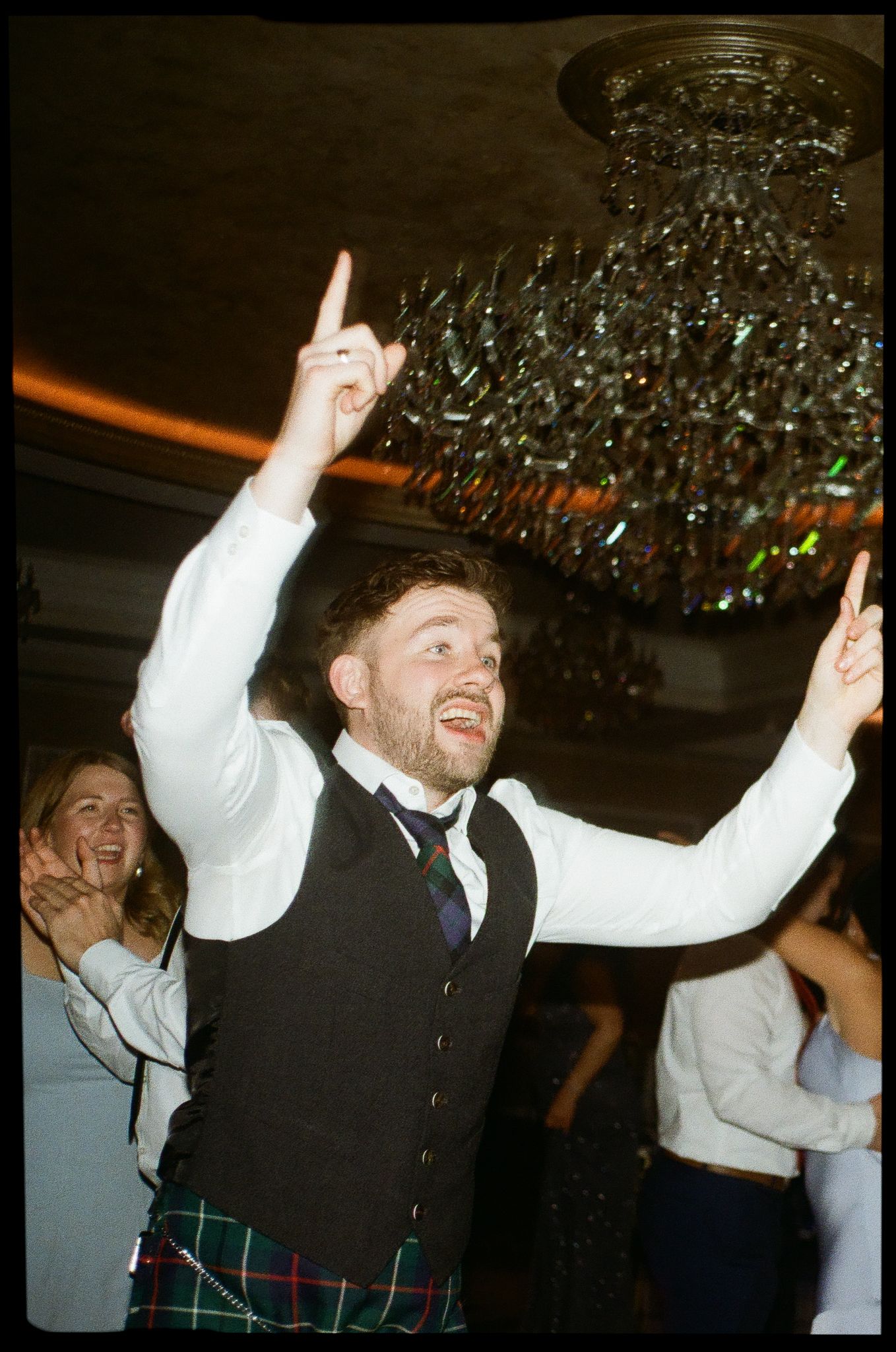 A cowboy hat-wearing dancer moves on the dance floor under warm string lights at an evening celebration.