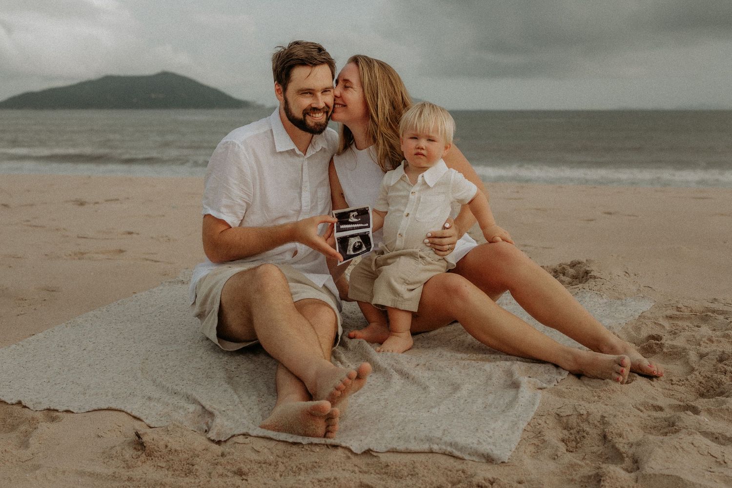 Family enjoying a tender moment together on the beach with a vintage camera.