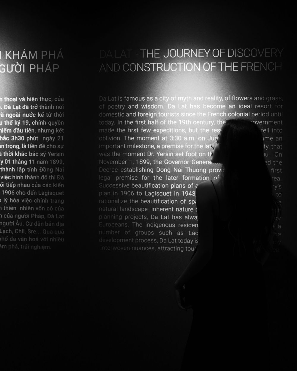 Silhouetted figure against wall of illuminated text in dark exhibition space.