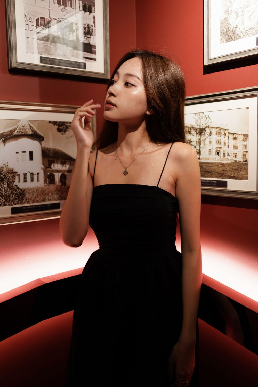 Artistic portrait in black dress against gallery wall with vintage photographs.