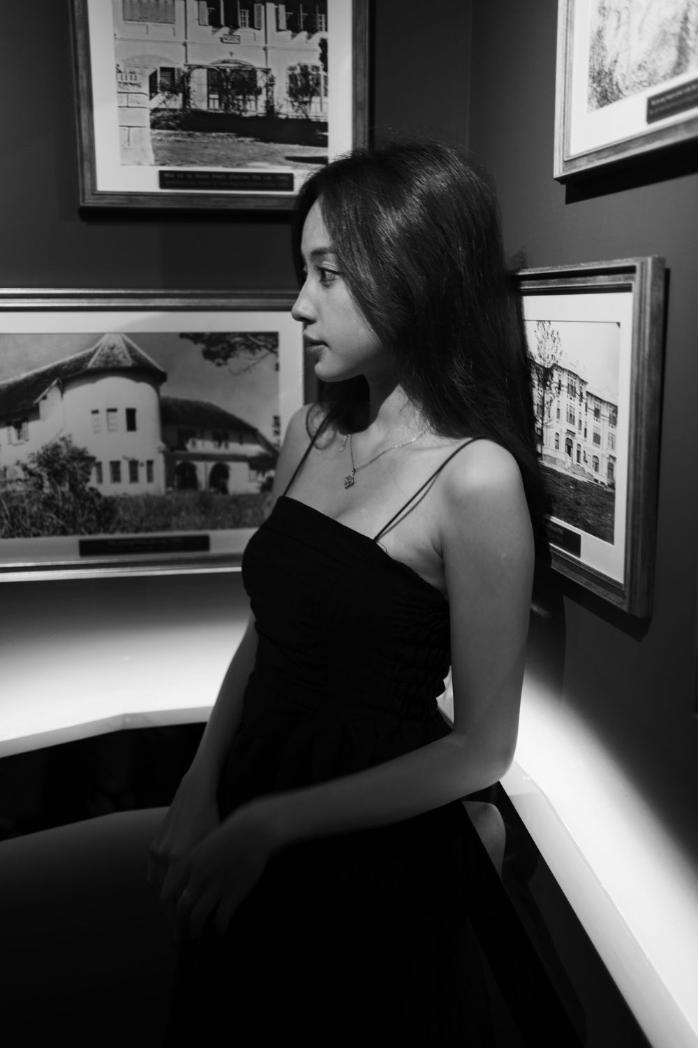 Black and white portrait in elegant dress against gallery wall with framed photographs.