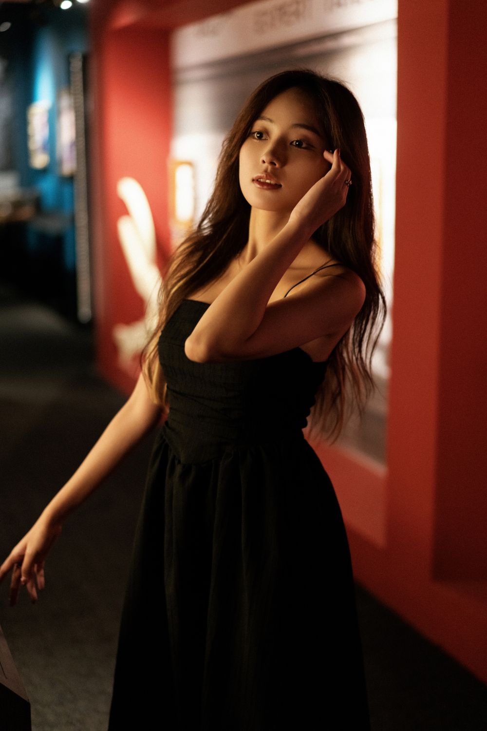 Elegant portrait in black dress against red wall with dramatic lighting.