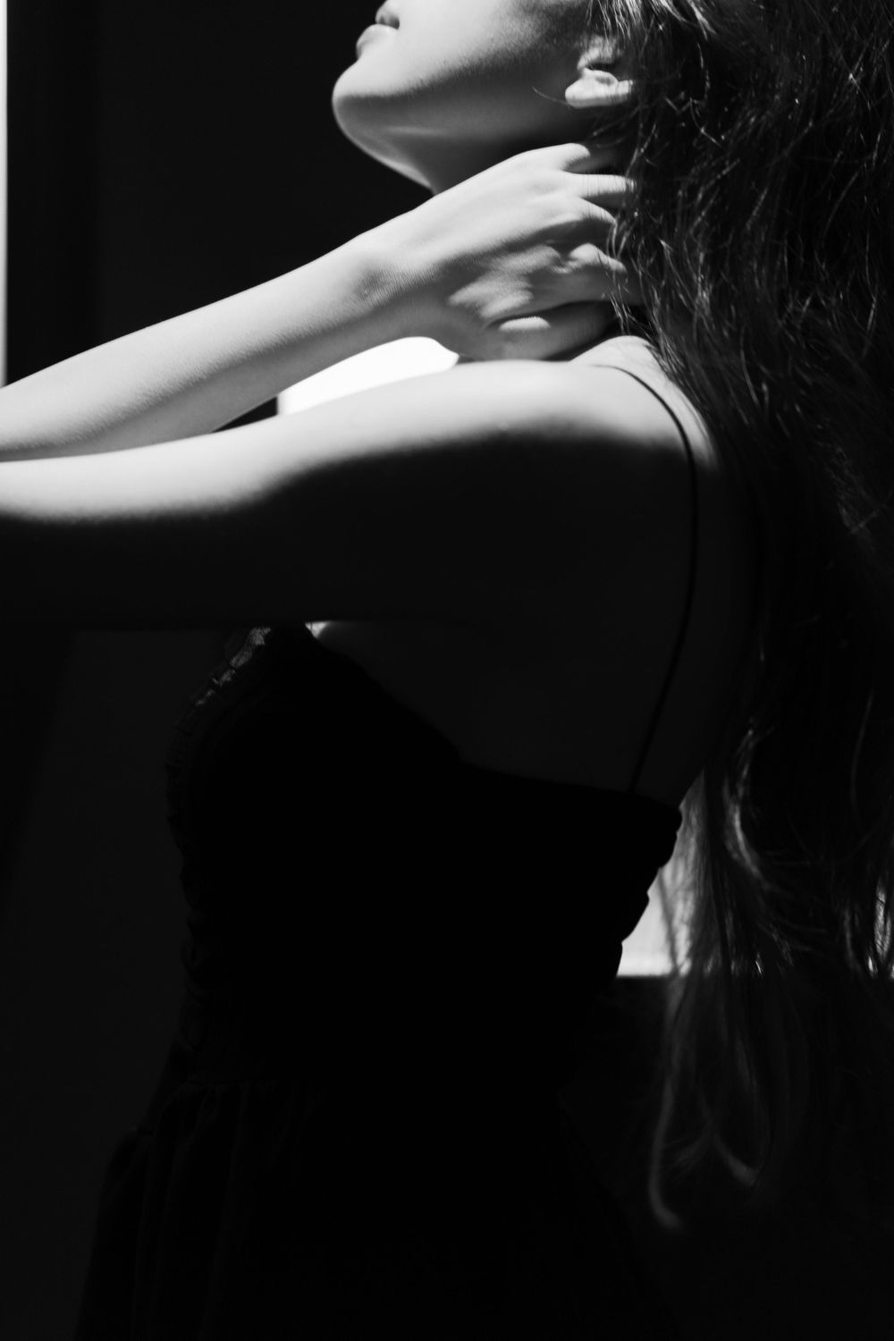 Artistic black and white portrait featuring dramatic lighting and elegant neck pose in dark setting.