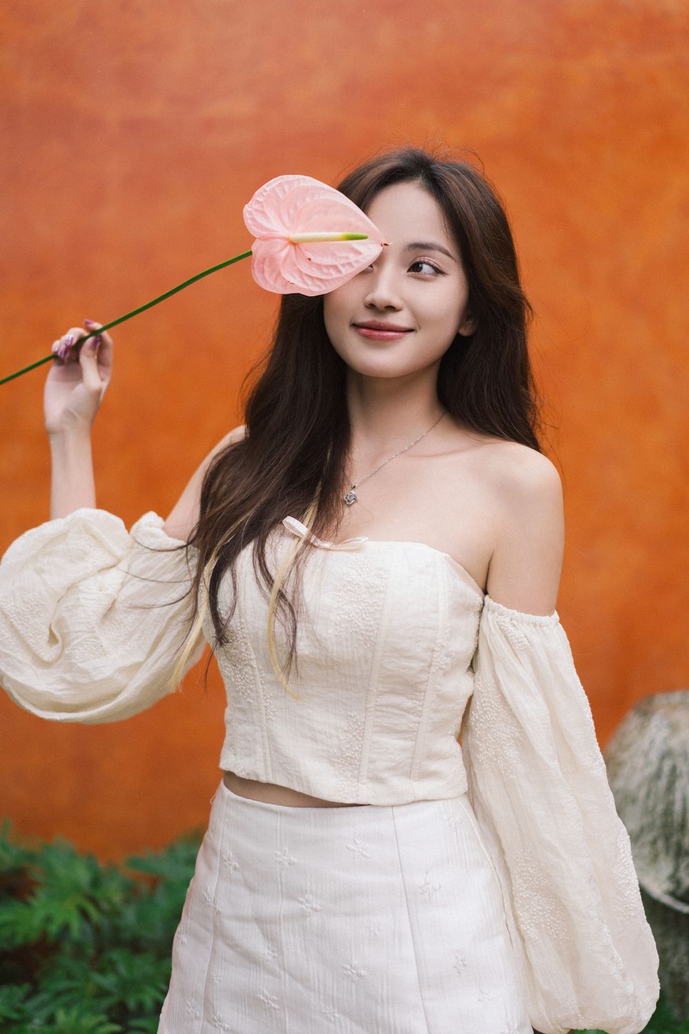 Dreamy portrait with pink anthurium flower against vibrant orange wall.
