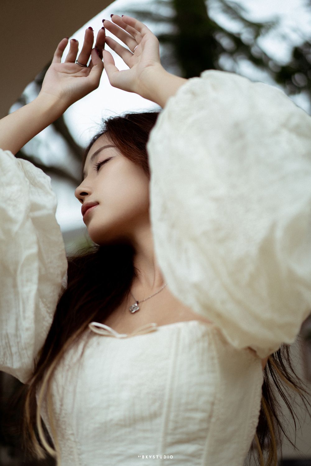 Ethereal portrait in white dress with dramatic flowing sleeves.