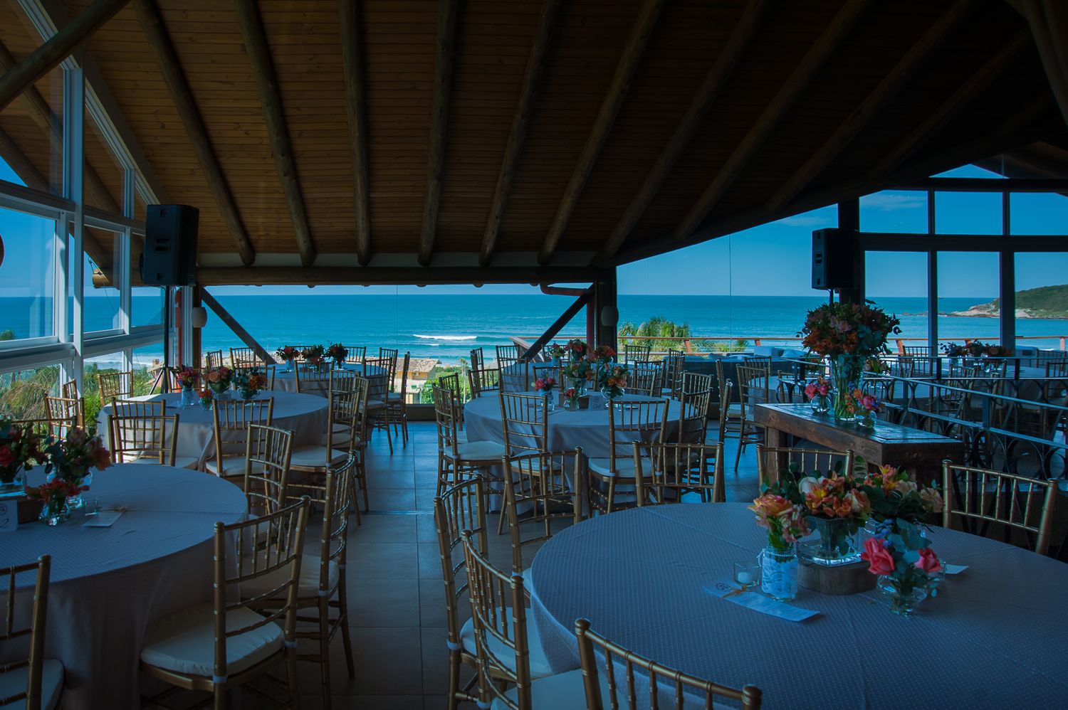 An elegant wedding reception venue with ocean views through large windows and round tables set for dining.