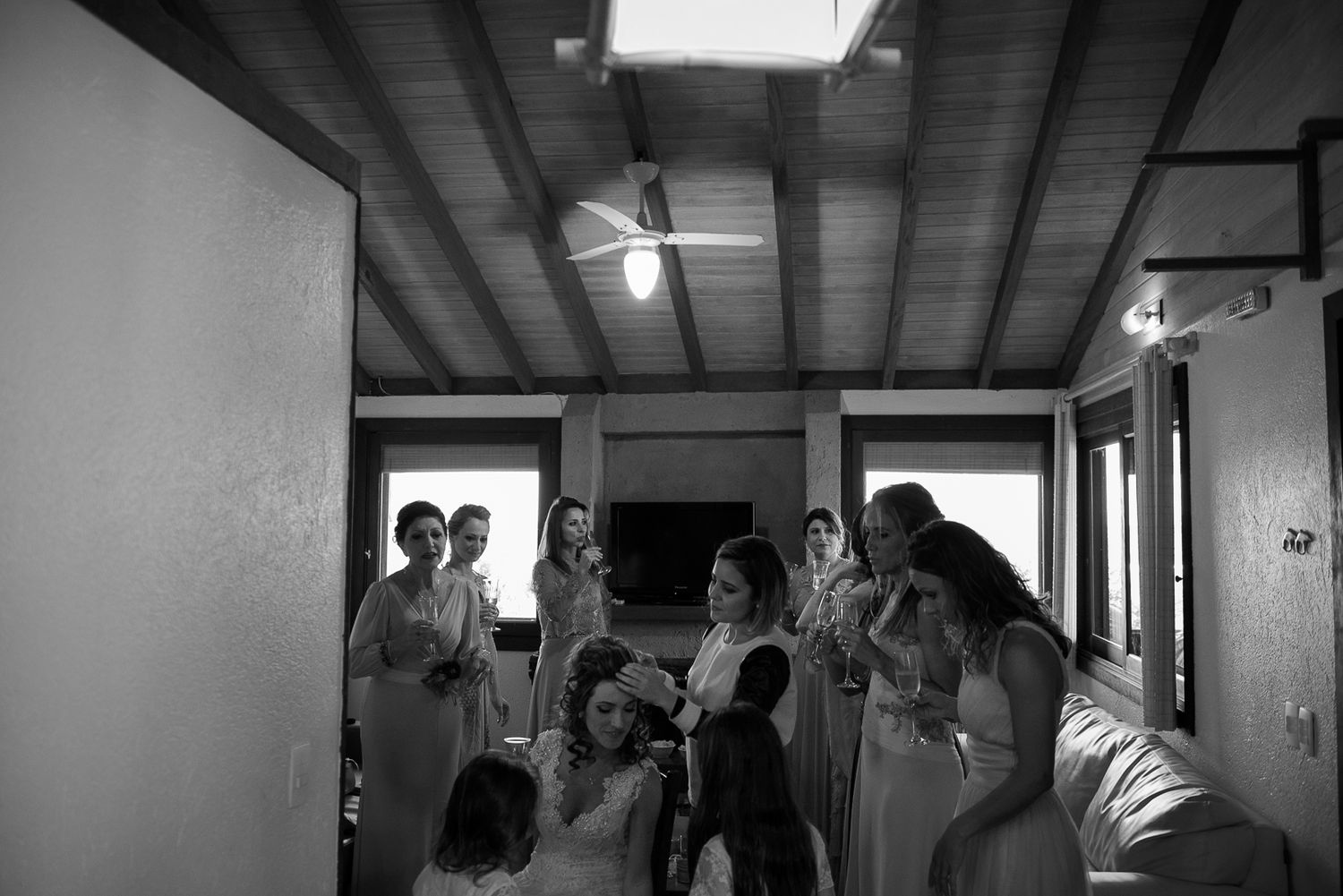 A group gathers in a hallway during wedding preparations captured in black and white photography.