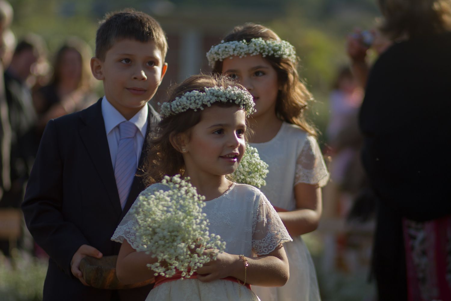 Young attendants wearing floral crowns at an outdoor wedding ceremony.