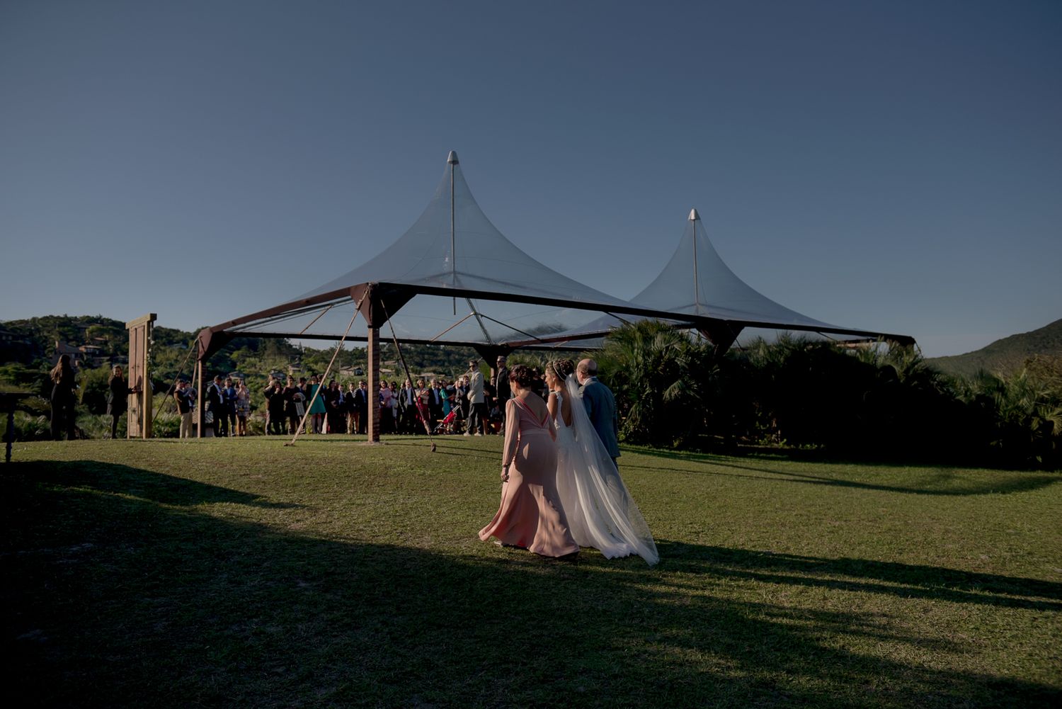 Outdoor wedding ceremony under modern tension fabric canopies against a blue sky.