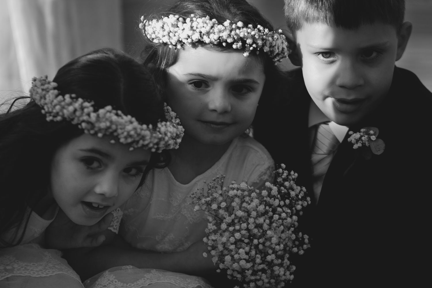 Children wearing floral crowns pose together in black and white photography.