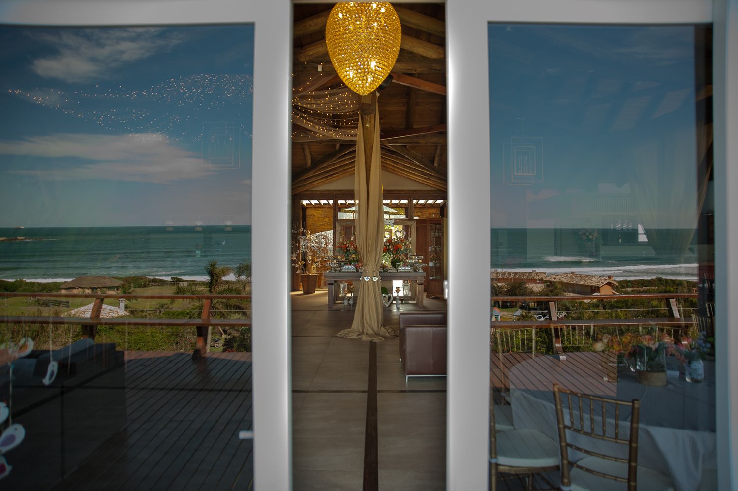 Ocean view through windows with a golden balloon reflection in the glass at a coastal venue.