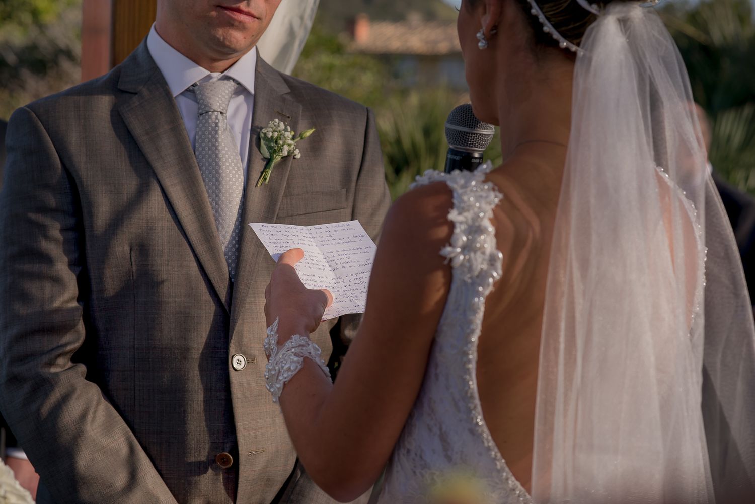 A couple exchanges vows at an outdoor wedding ceremony, with the groom reading from a card while holding a microphone.
