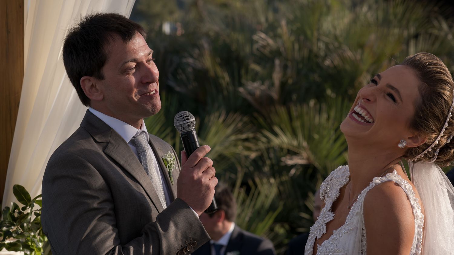 A joyful wedding ceremony moment under a decorated canopy as vows are exchanged with microphones.