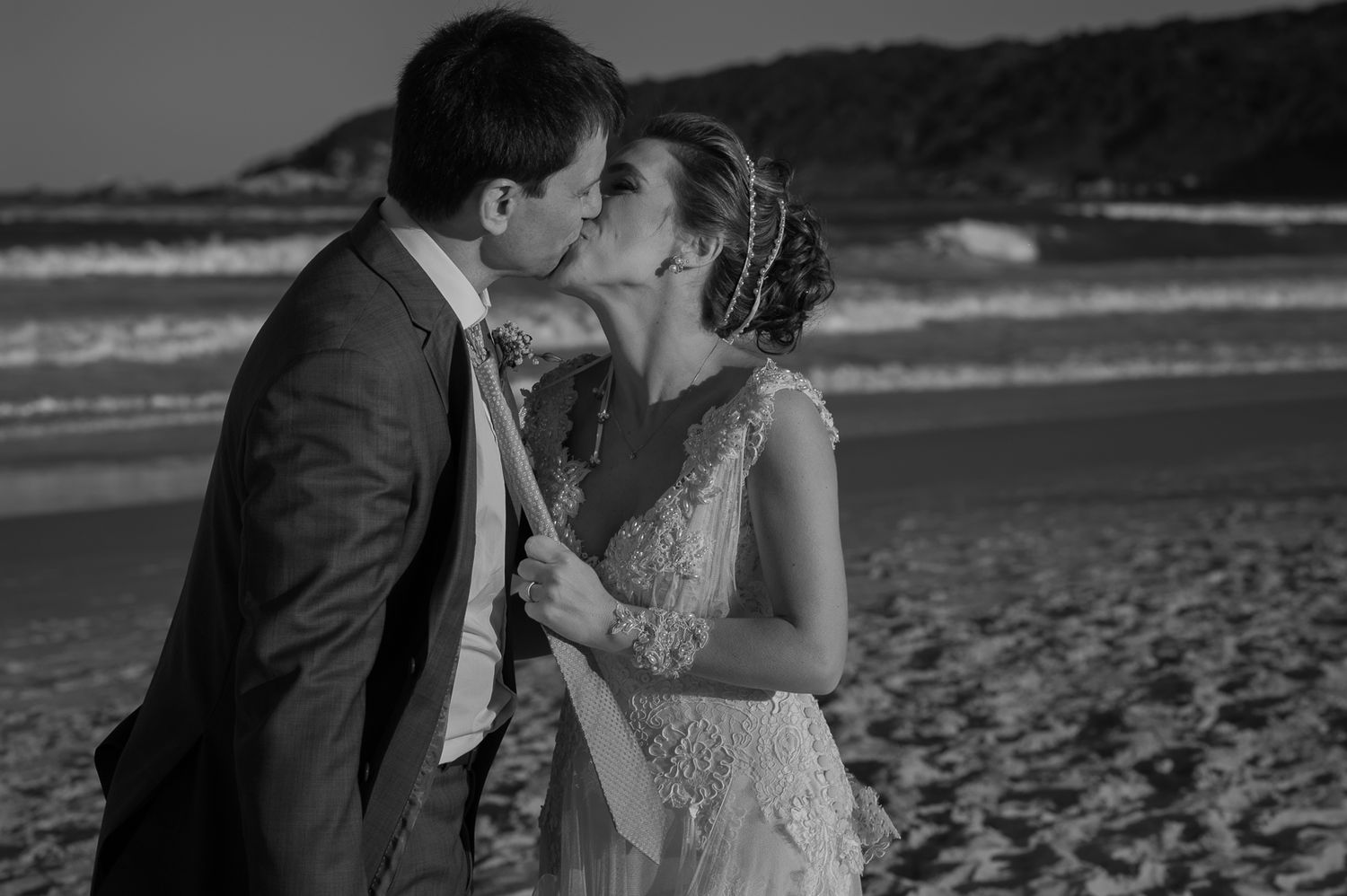 A romantic black and white beach wedding photo of a couple sharing a kiss by the ocean.