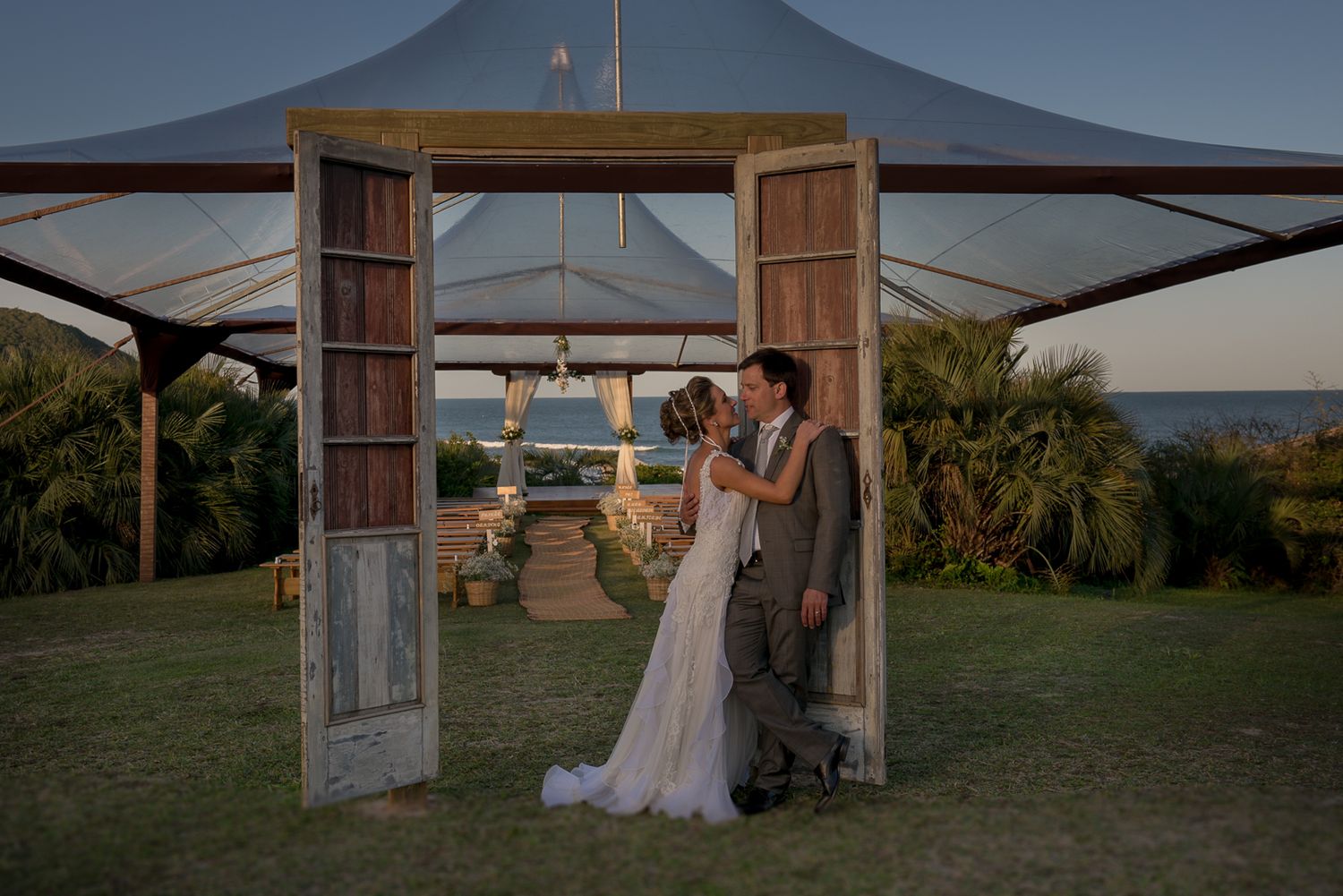 A couple shares an intimate moment under a wooden archway at their oceanfront wedding venue.