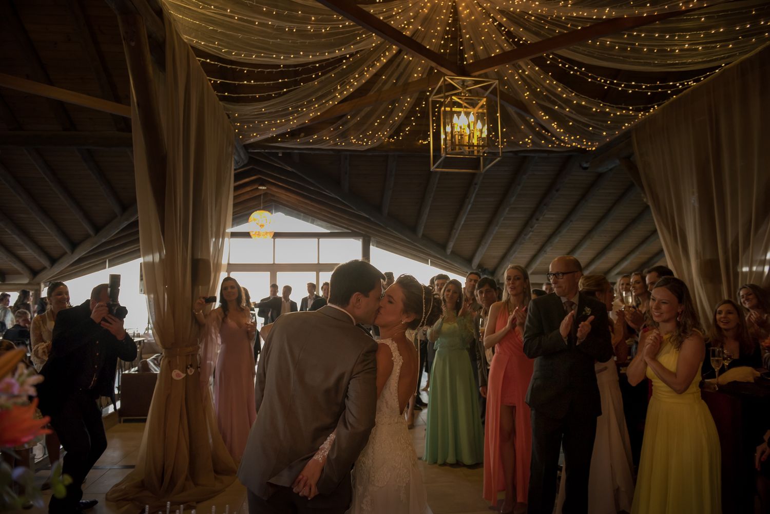 Wedding reception in a barn-style venue with string lights and gathered guests on the dance floor.