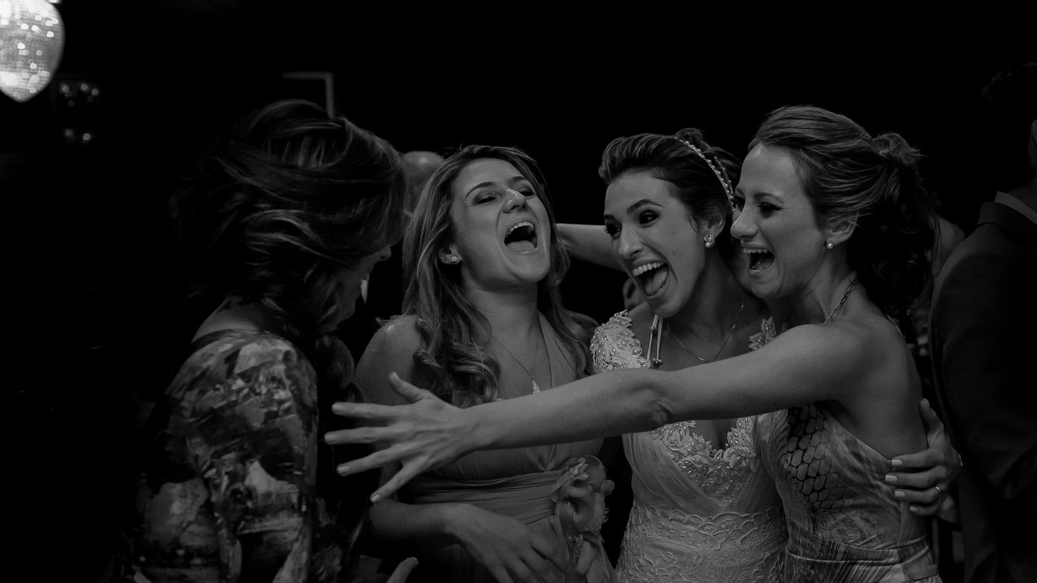 Black and white photo of wedding guests sharing an excited group embrace on the dance floor.
