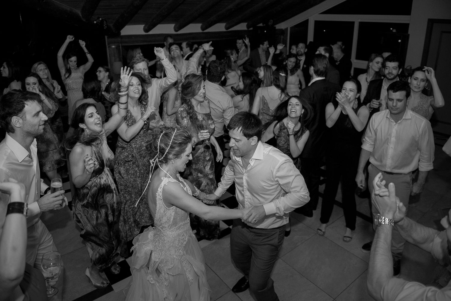 Black and white photo of a lively wedding reception with guests dancing and celebrating.