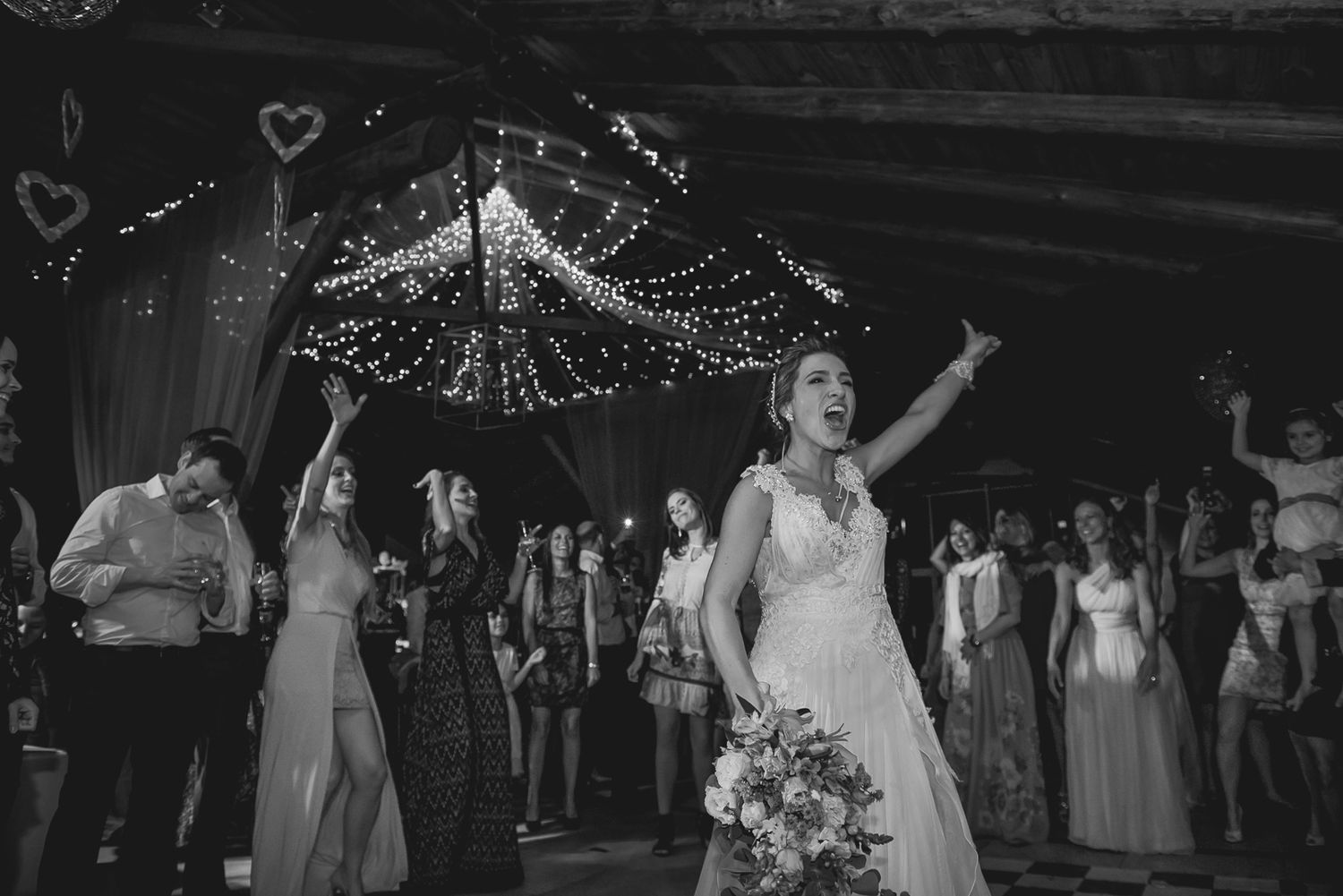 Black and white photo of a wedding reception with twinkling lights and celebratory atmosphere.